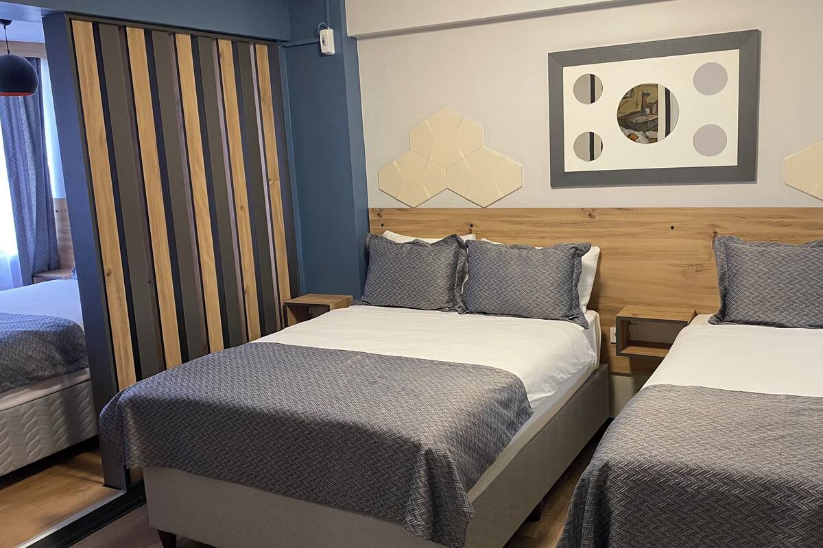 Ett hotellrum med två sängar, en sänggavel i trä, en geometrisk väggdekoration och ett fönster med gardiner.