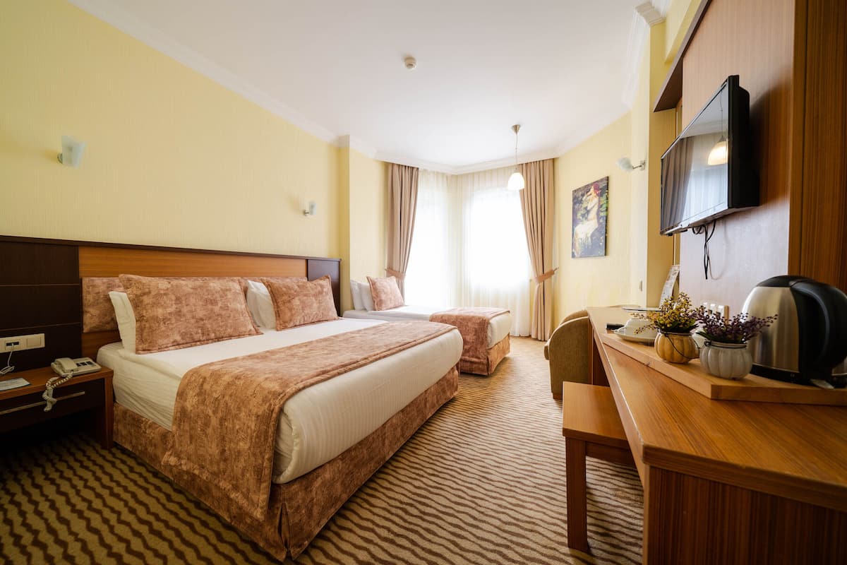 Ein Hotelzimmer mit einem großen Bett, einem Schreibtisch mit Wasserkocher und einem an der Wand montierten Fernseher.