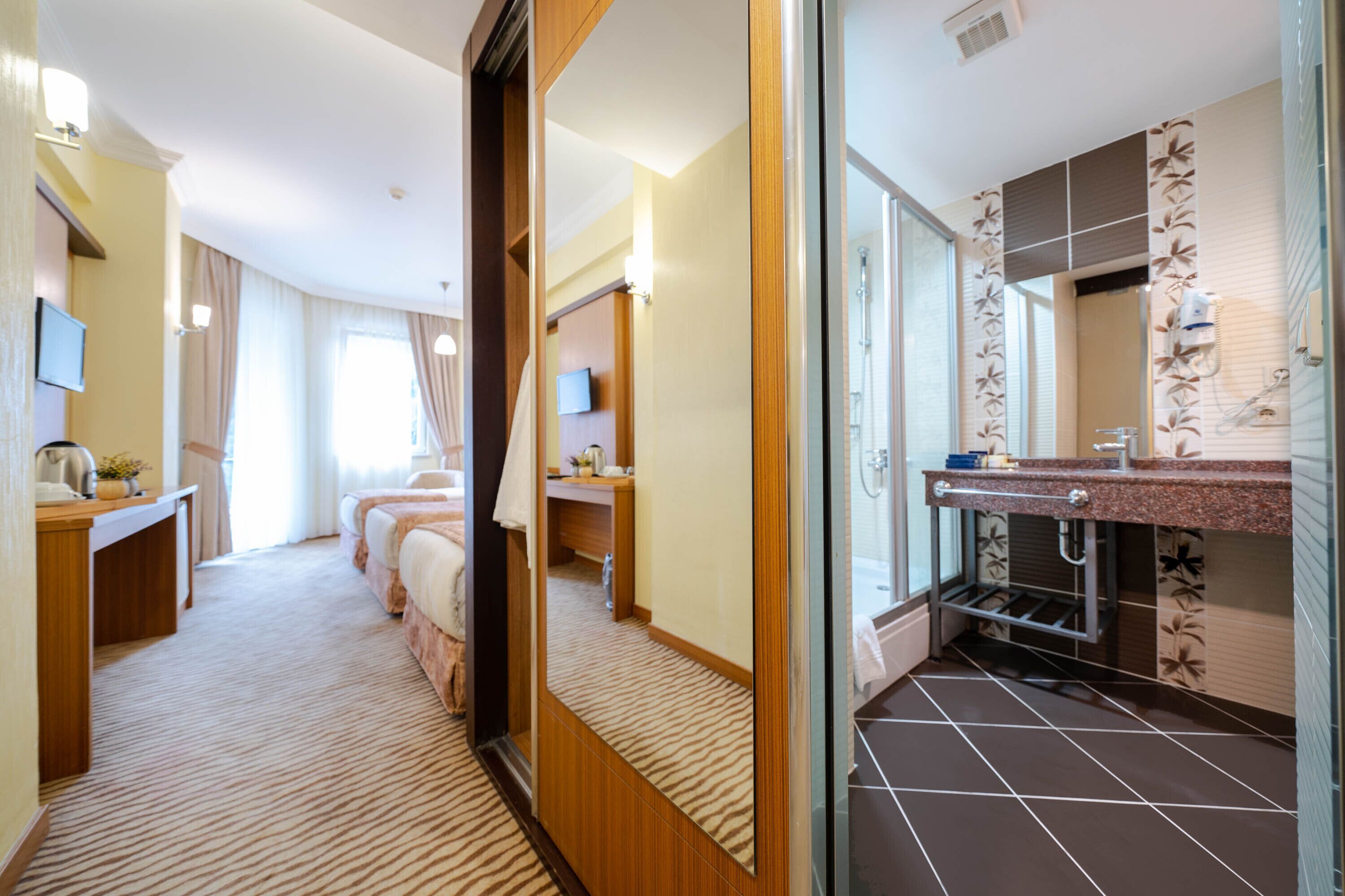 Habitación de hotel con un espejo grande, un escritorio de madera, una cama y un baño con ducha y lavamanos.