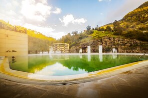 A swimming pool with a clear view of the surrounding landscape, including a building and a rocky hillside. - Ridos Thermal Hotel Spa (Ikizdere)