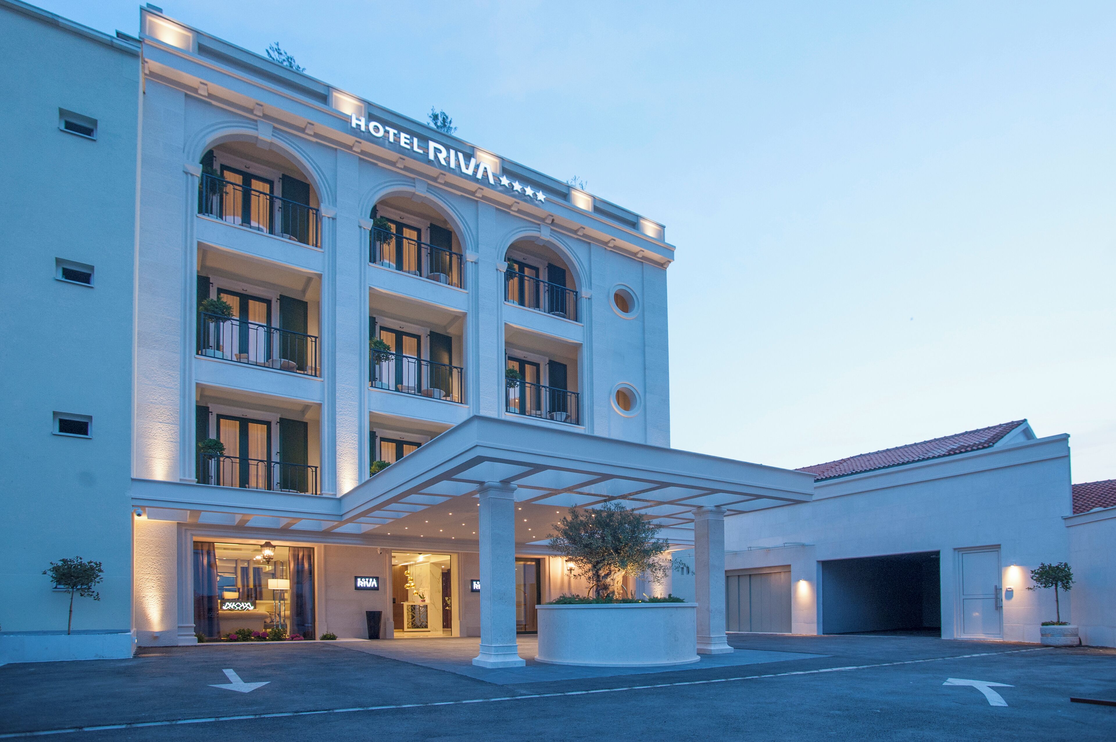 A multi-story hotel with a classic architectural design, featuring a central entrance with a covered walkway and a parking area in front.