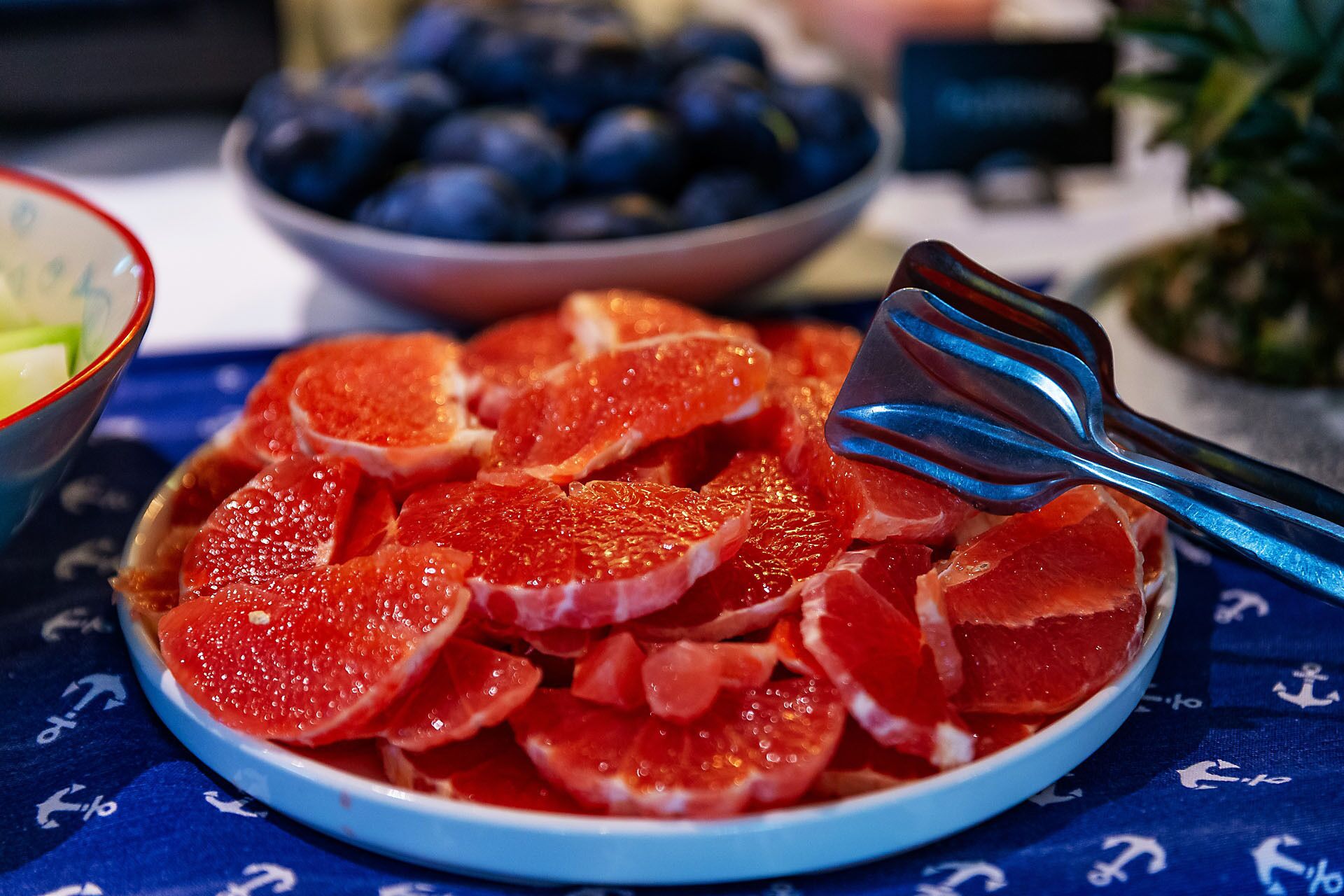 Un tazón de pomelo en rodajas con un utensilio de metal sobre una mesa con mantel azul.