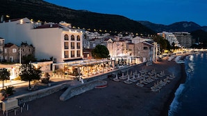 Un hotel frente al mar con terraza en la playa, edificios de piedra y vistas al océano.