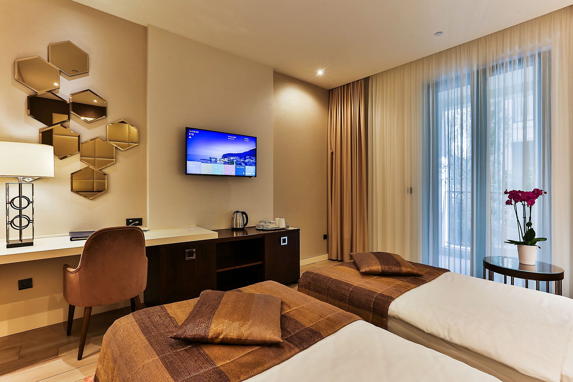 Habitación de hotel con dos camas, un escritorio, un televisor y una ventana con cortinas.