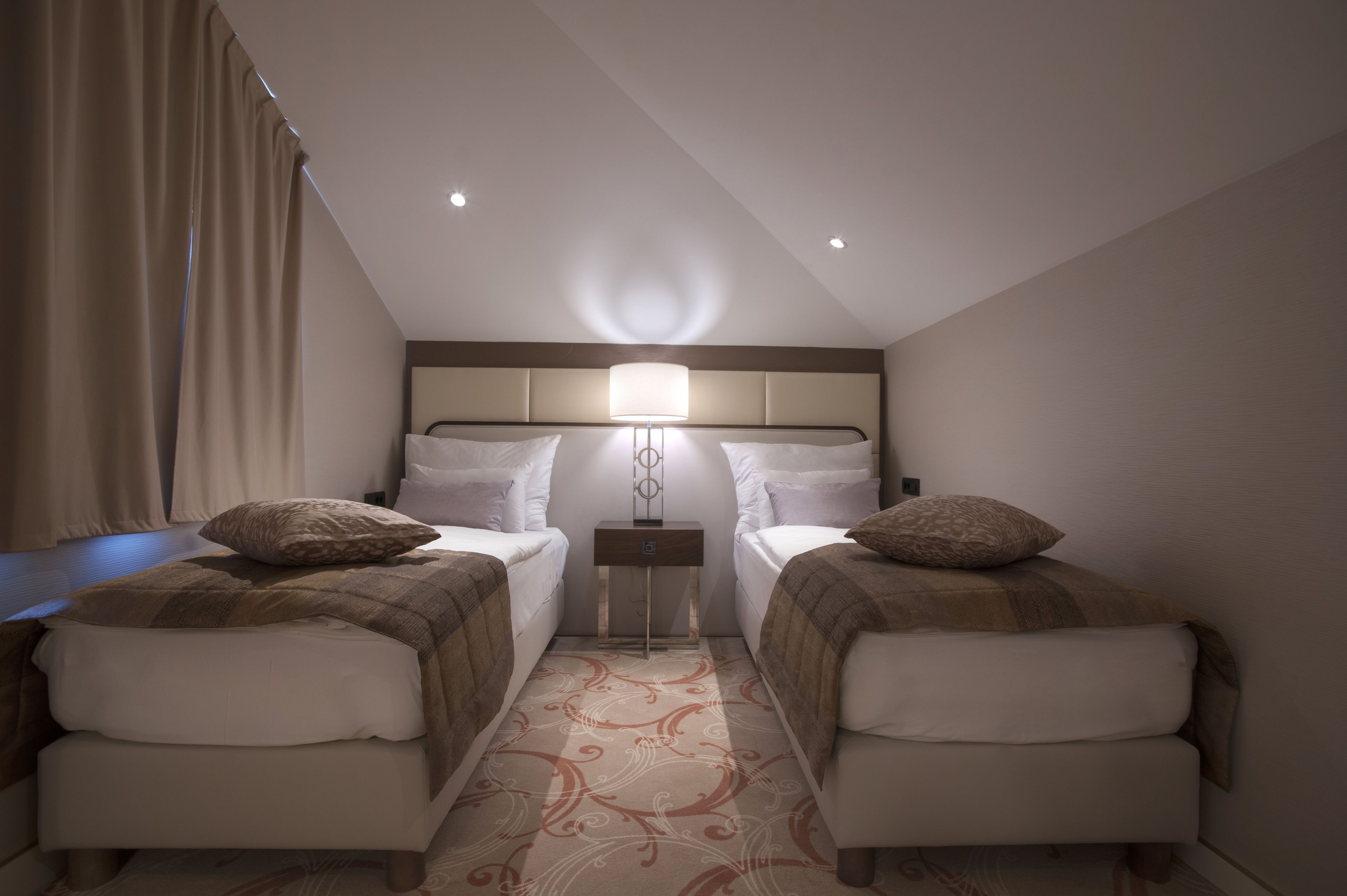 A hotel room with two beds, a nightstand, a lamp, and a patterned carpet.