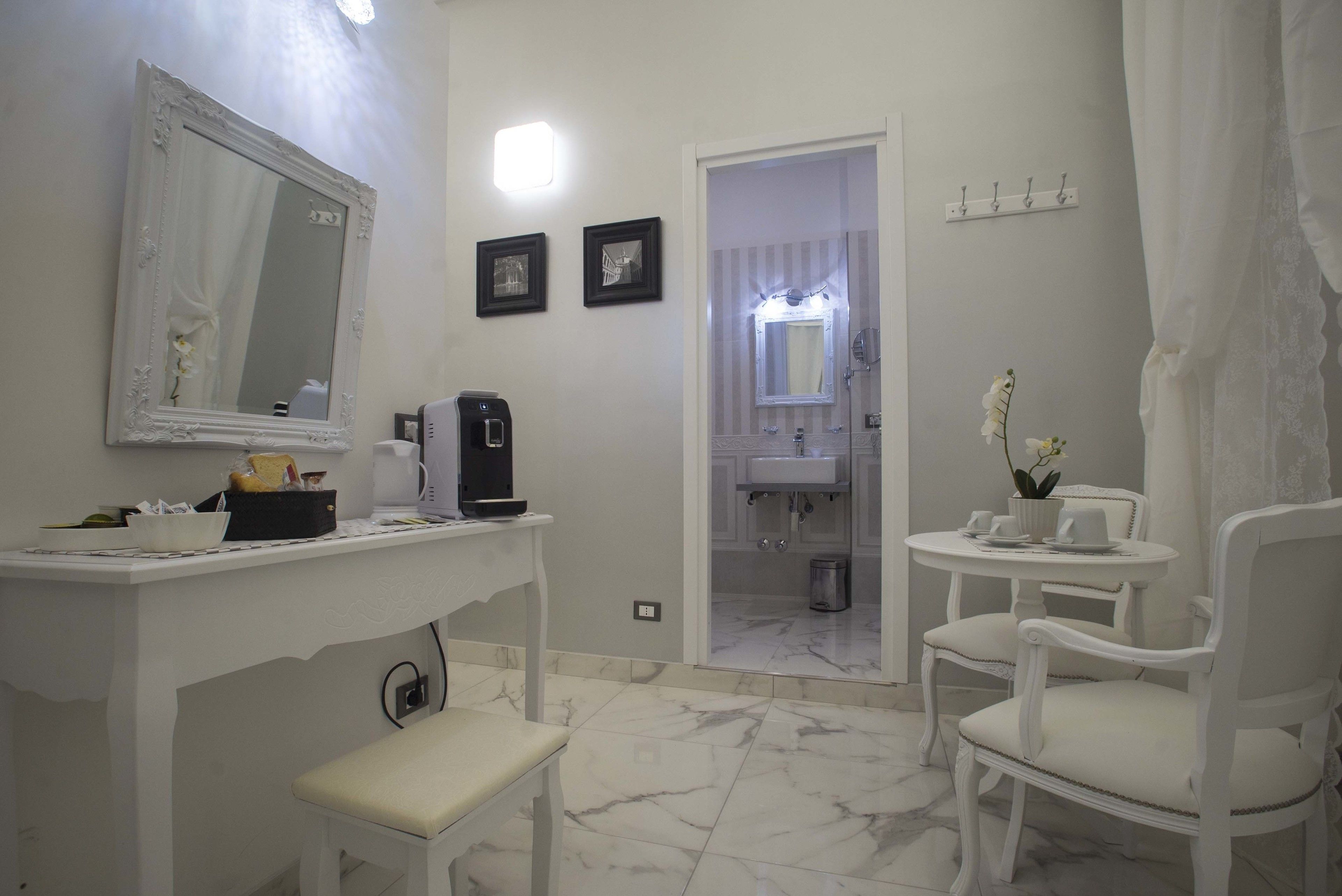 A bathroom with a white vanity, a large mirror, a coffee maker, and two chairs.