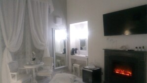 Een hotelkamer met een open haard, een aan de muur bevestigde televisie, een kleine tafel met een stoel en een grote spiegel.