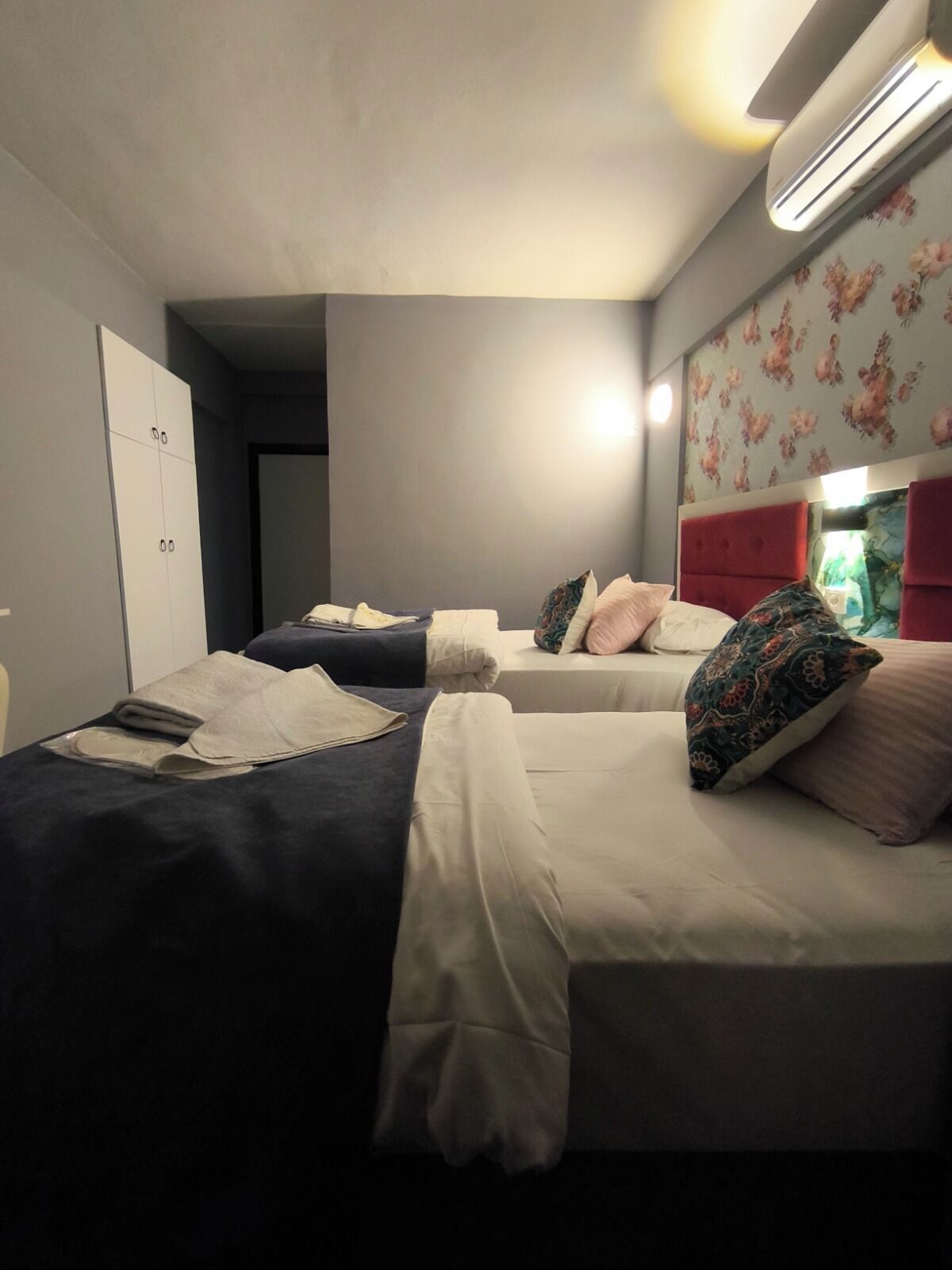 Habitació d'hotel amb dos llits, un armari i un fons de pantalla amb motius florals.