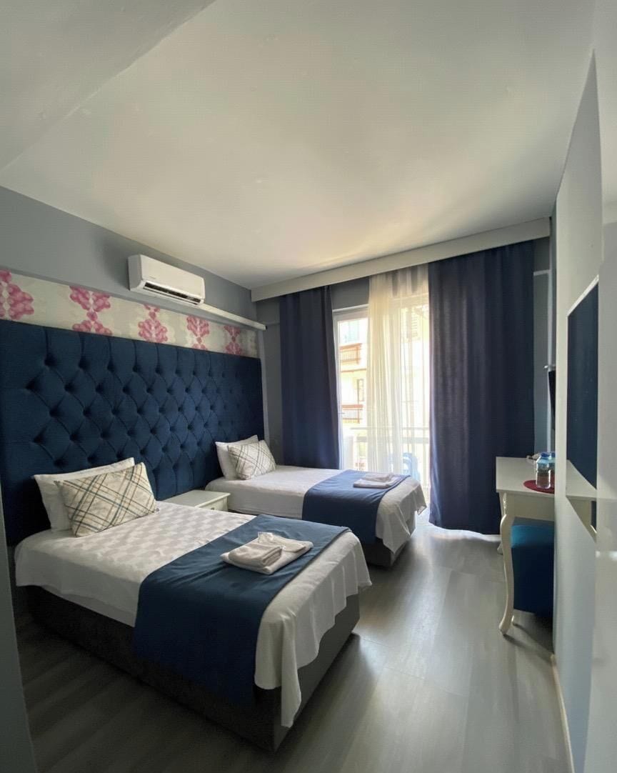 A hotel room with two beds, a desk, a TV, and an air conditioning unit.