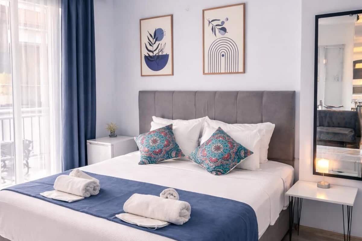 A modern hotel room with a large bed, a bedside table, a mirror, and artwork on the wall.