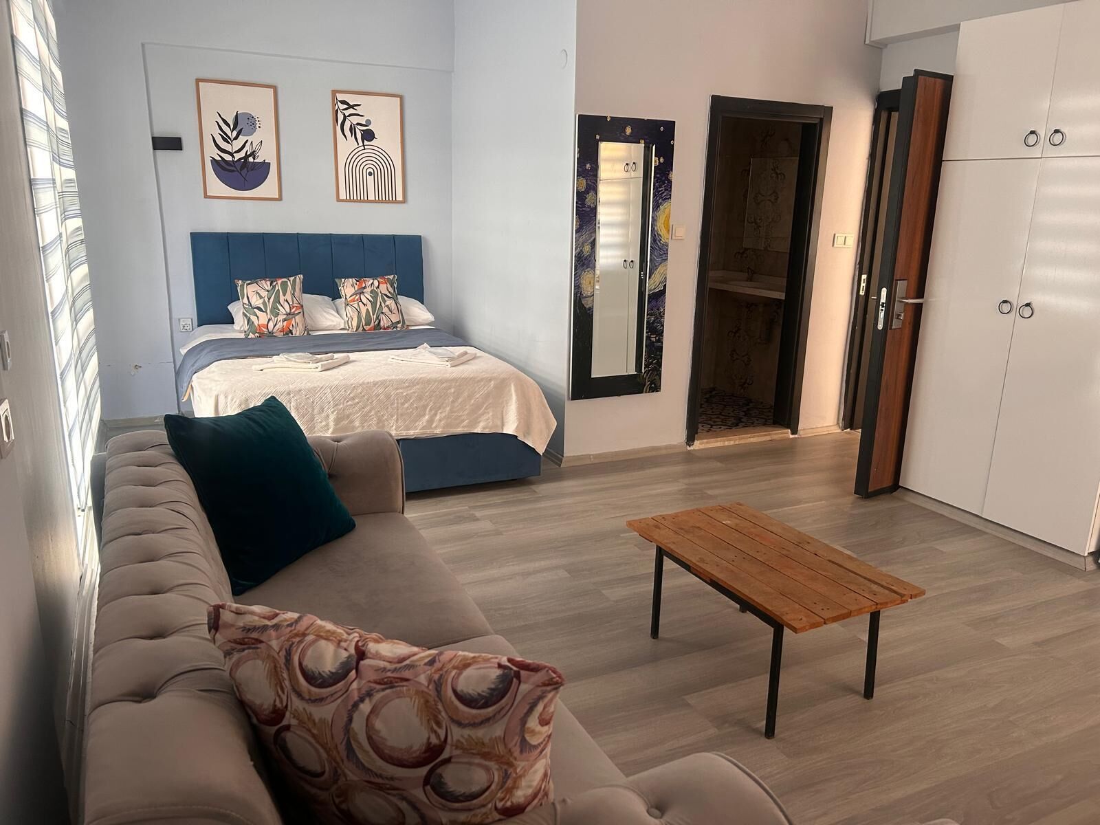 A modern bedroom with a bed, a sofa, a wooden table, and a wardrobe.