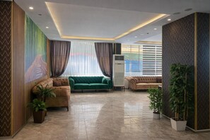 A spacious lobby with a green sofa, two brown sofas, a large window with sheer curtains, and a modern ceiling design. - AKMAN CITY HOTEL (Kusadasi)