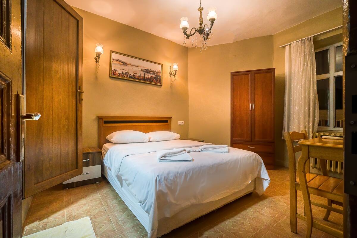 A hotel room with a large bed, wooden wardrobe, and a dining table.
