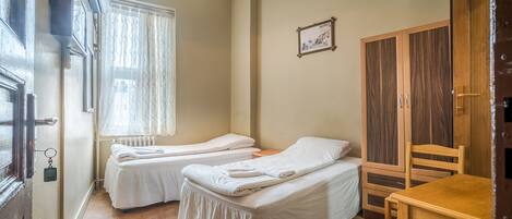 A room with two single beds, a wooden wardrobe, a small table, and a radiator near the window.