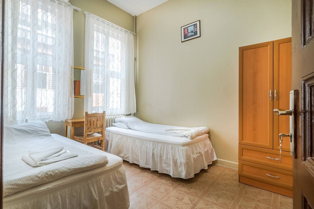 A bedroom with two single beds, a wooden wardrobe, a chair, and a radiator.