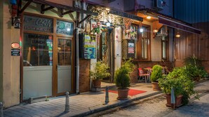A restaurant with outdoor seating, potted plants, and a sign indicating breakfast, lunch, and dinner services. - Yeni Hotel (Istanbul)