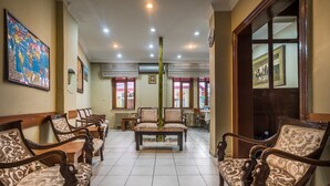 A hotel lobby with rows of wooden chairs and tables, a central decorative pillar, and framed pictures on the walls. - Yeni Hotel (Istanbul)