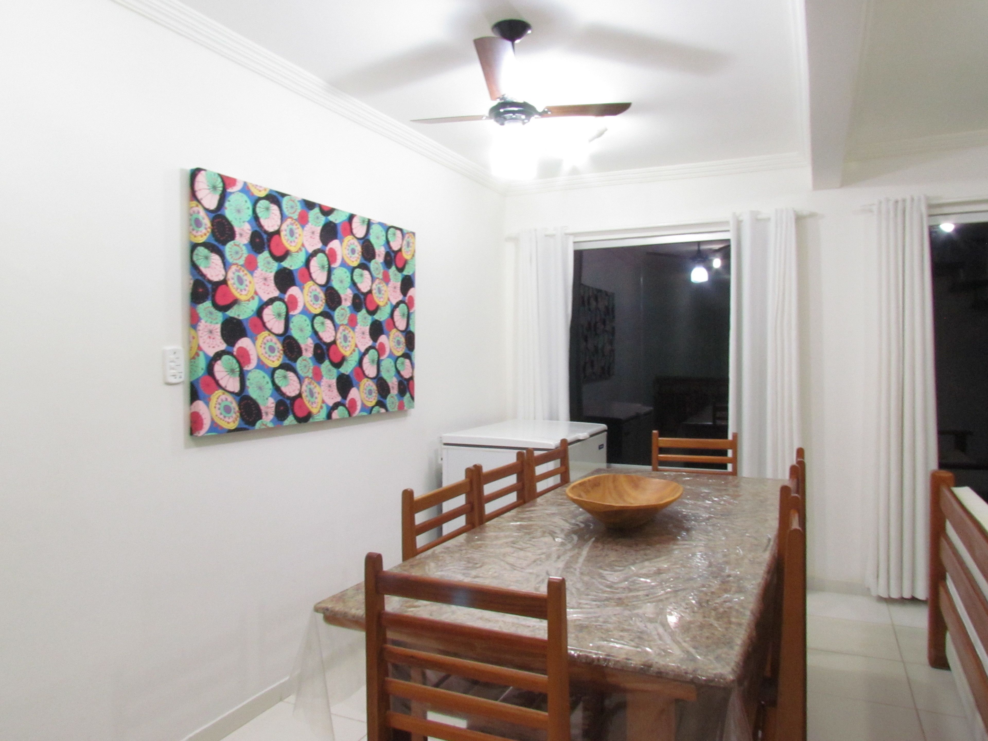 A dining area with a table, chairs, a ceiling fan, and a colorful wall decoration.