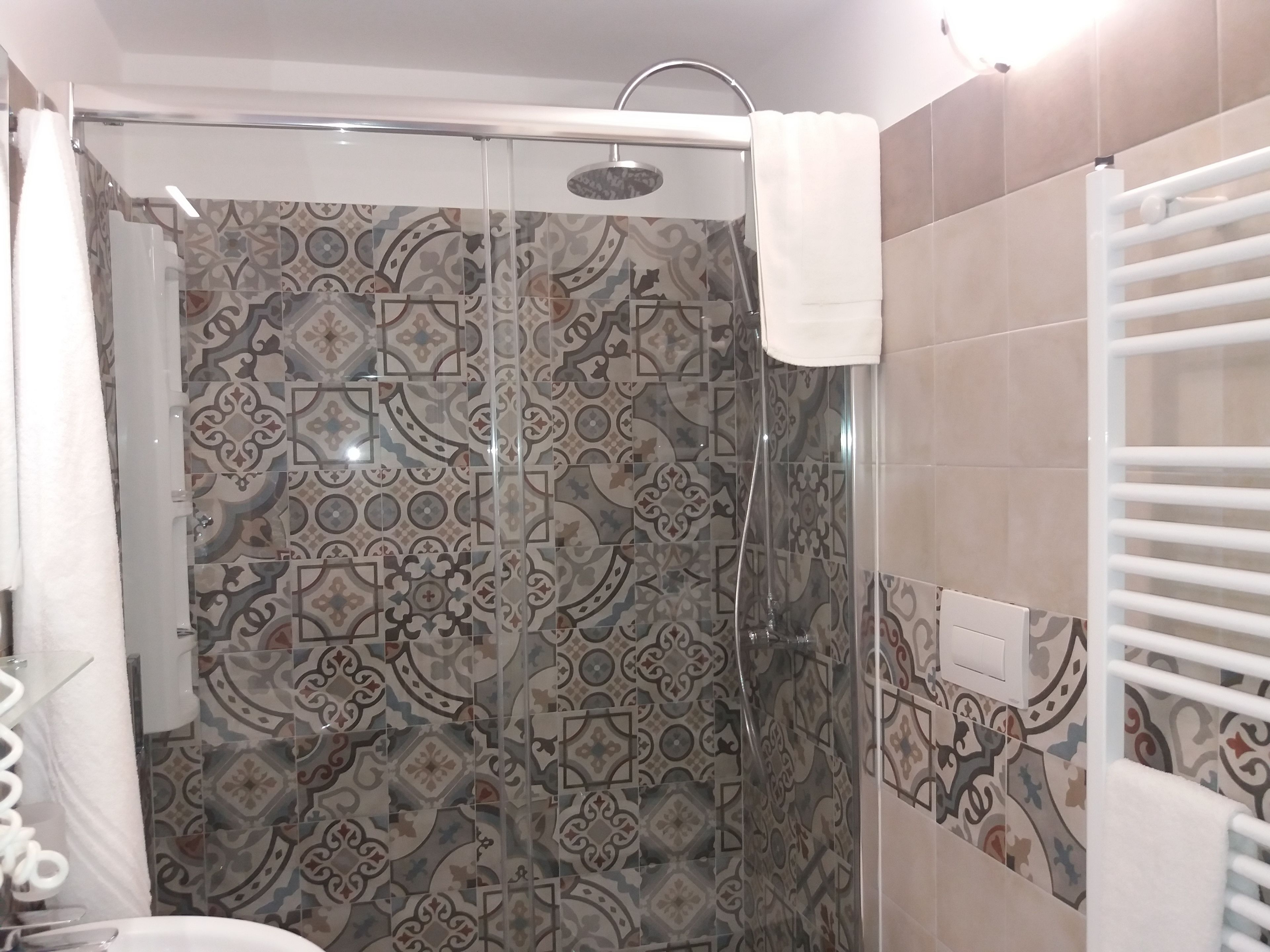 A shower with a glass door, patterned tiles, and a white towel hanging on the wall.