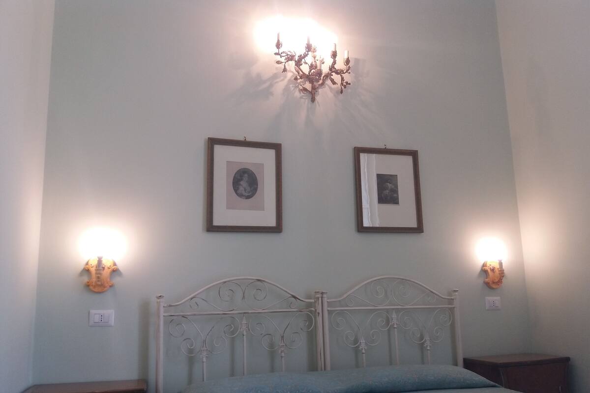 Ein Schlafzimmer mit einem Metallbettgestell, zwei gerahmten Bildern an der Wand und Wandleuchten.