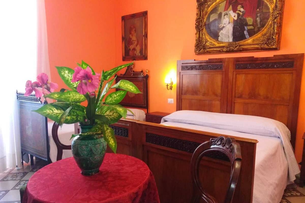 Ein Zimmer mit einem Bett, einem hölzernen Schminktisch, einem Tisch mit roter Tischdecke und einer grünen Vase mit Blumen.