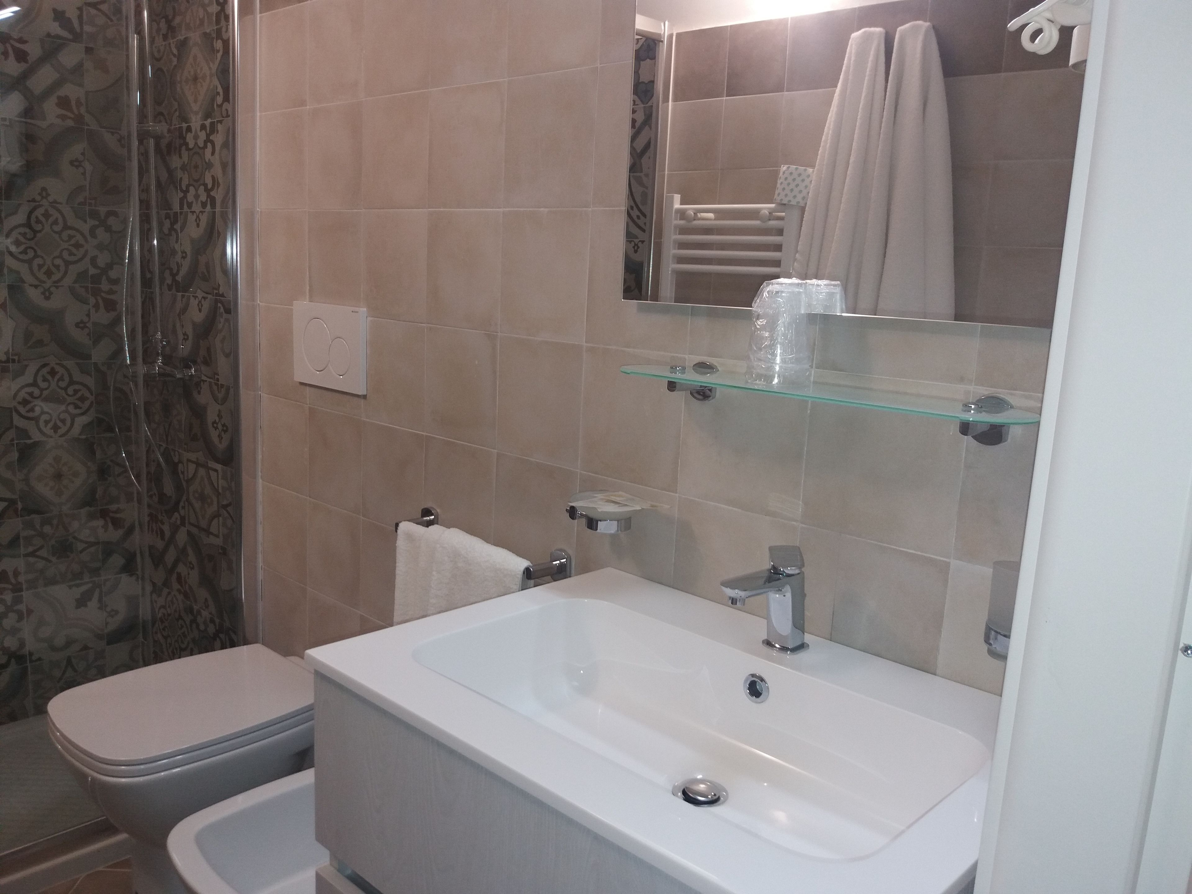 A bathroom with a white sink, a glass shelf, a towel rack, and patterned tiles.
