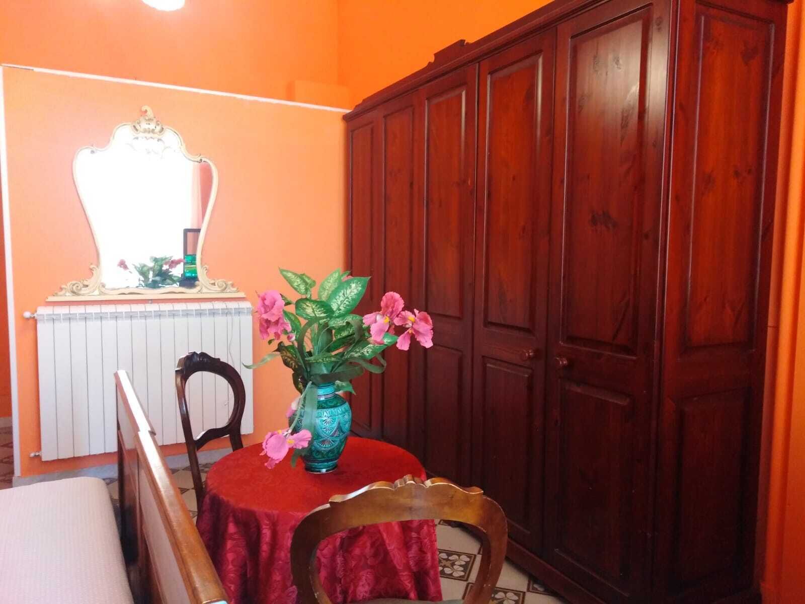 Ein Zimmer mit einem Holzkabinett, einem Tisch mit rotem Tischlein und einem Stuhl.