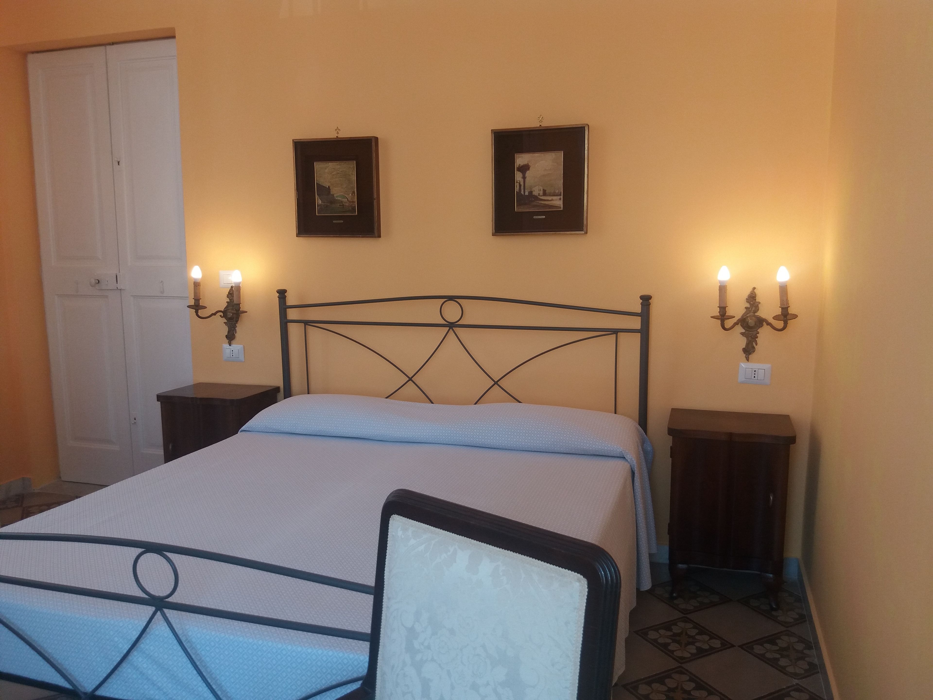 A bedroom with a bed, two bedside tables, a chair, and two wall-mounted sconces.