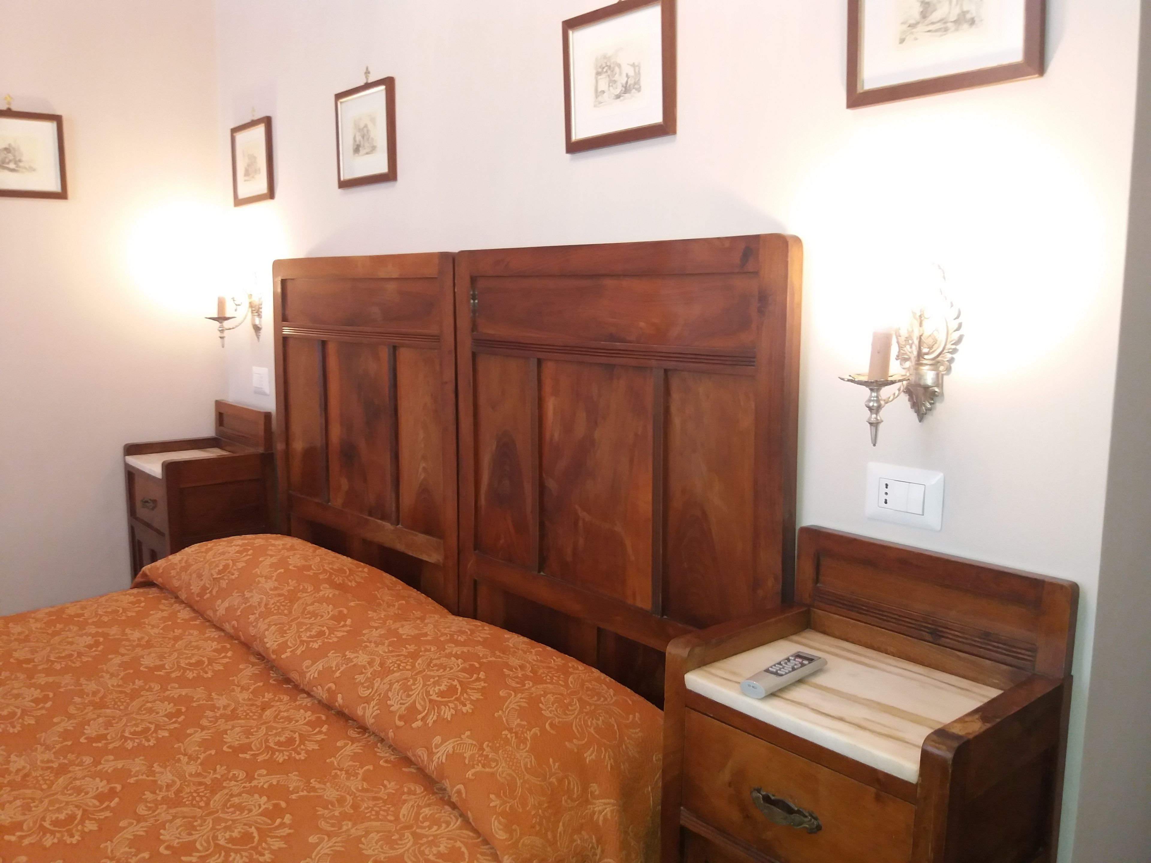 A bedroom with a wooden bed, a bedside table with a remote control, and framed pictures on the wall.