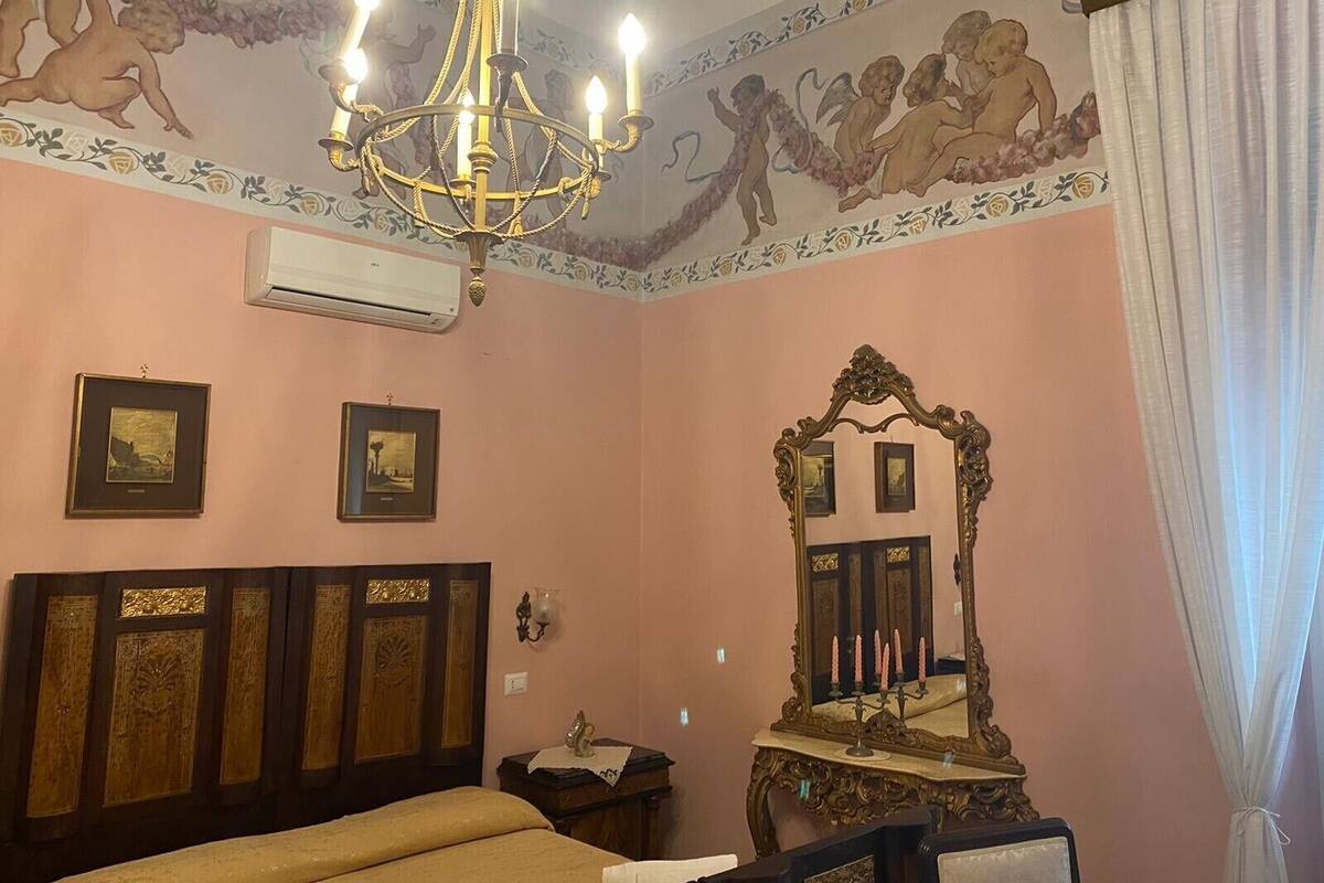 Ein Zimmer mit einem großen Bett, einer Kristallleuchter, einem Spiegel mit Kerzen und Wandbildern.