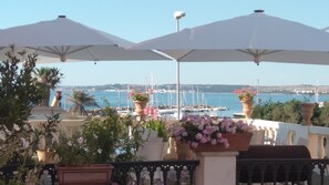 Una terraza con sombrillas blancas, plantas en macetas y vistas a barcos en un puerto deportivo.