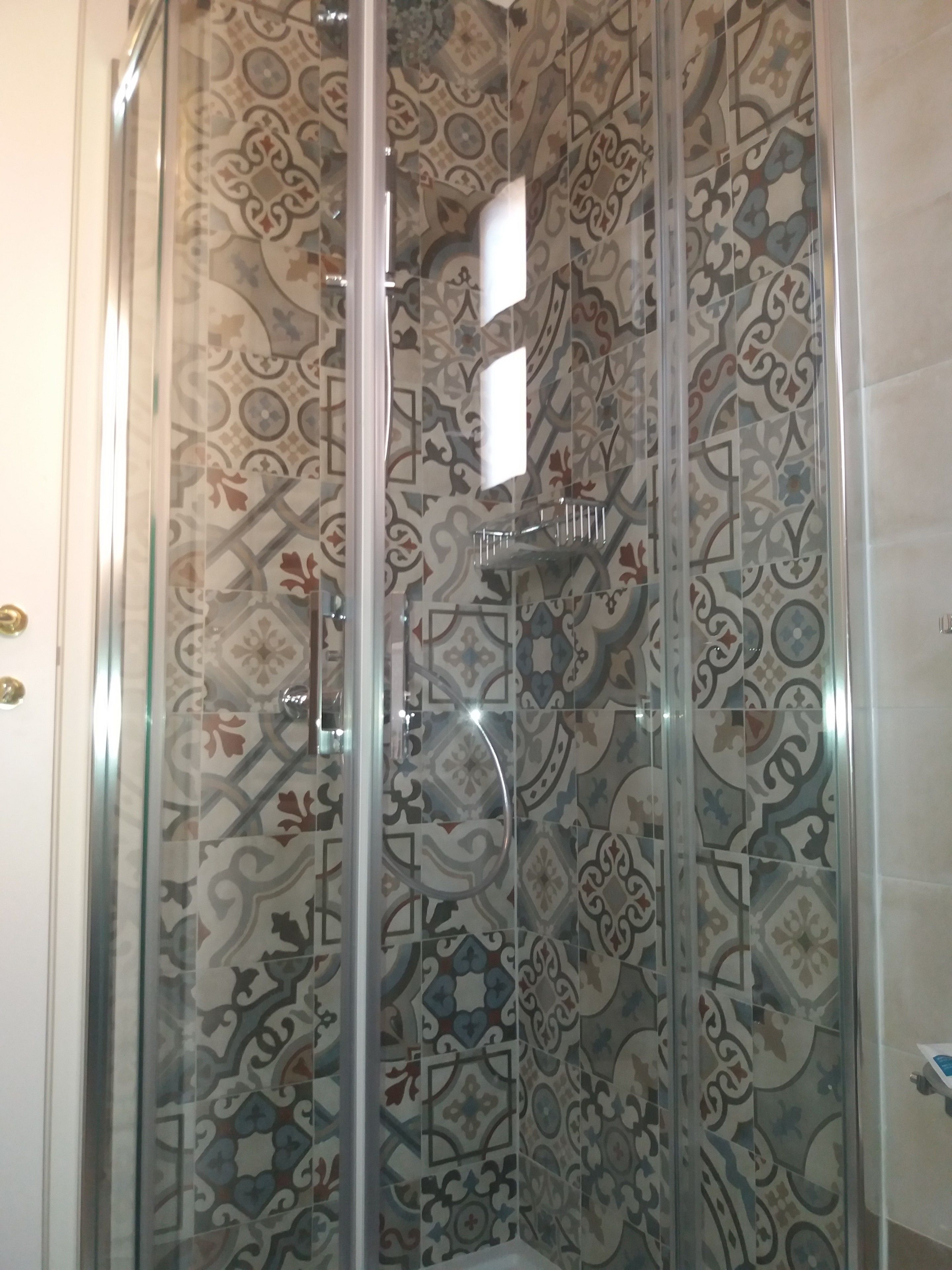 A shower with a glass door and patterned tiles.