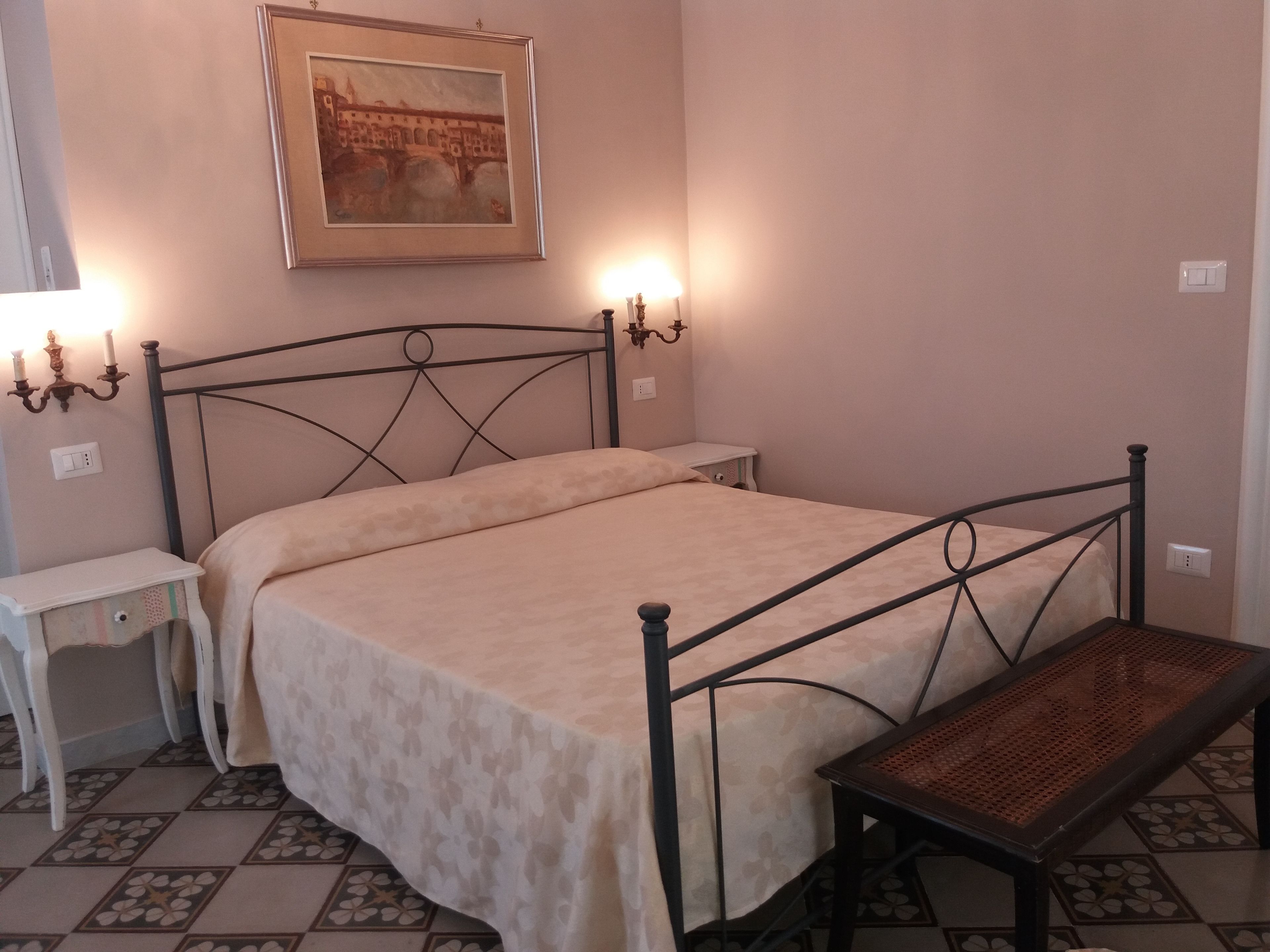 A bedroom with a bed, bedside tables, a nightstand, a lamp, and a painting on the wall.