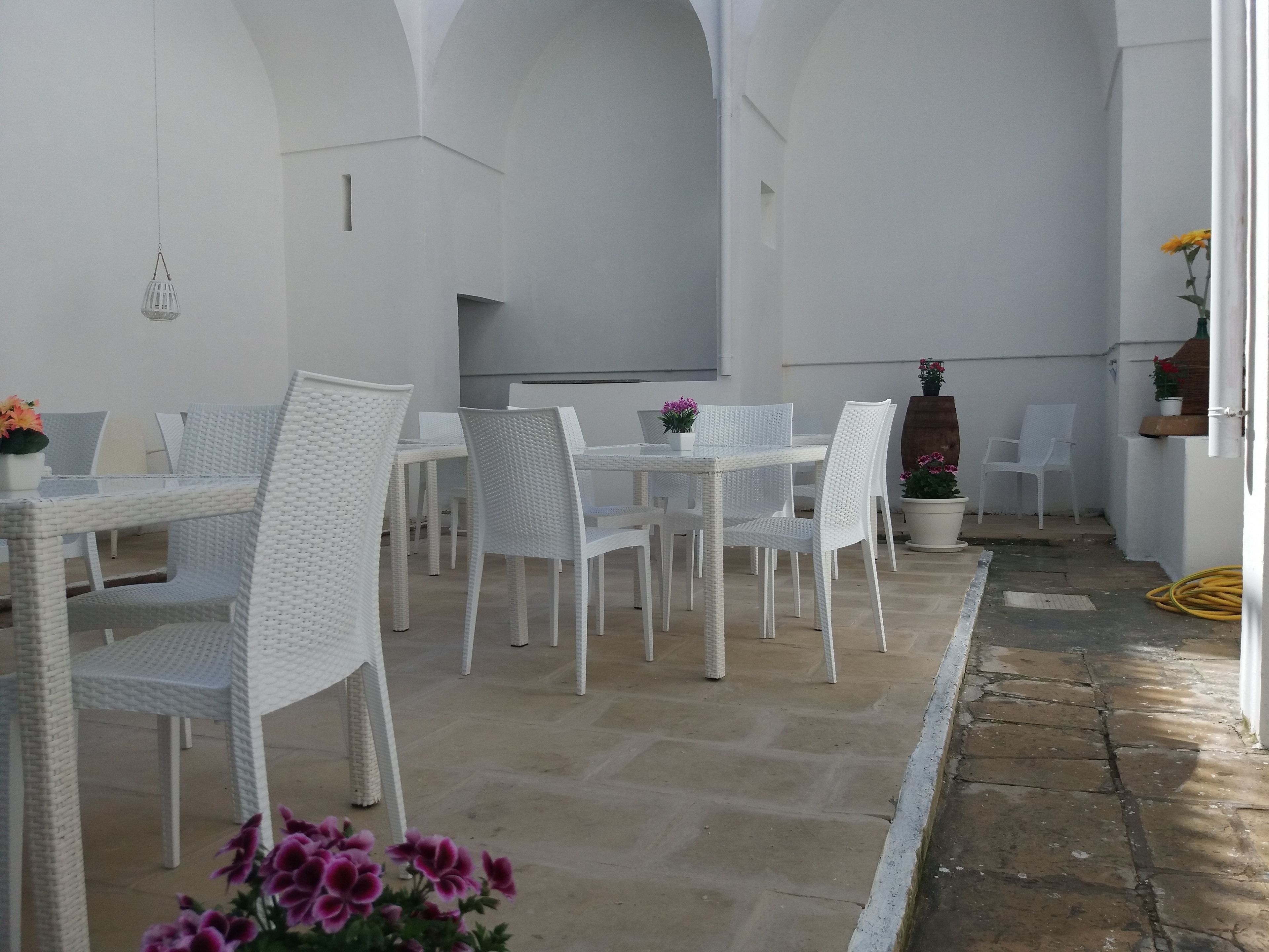 A patio with white wicker furniture, potted plants, and a stone floor.