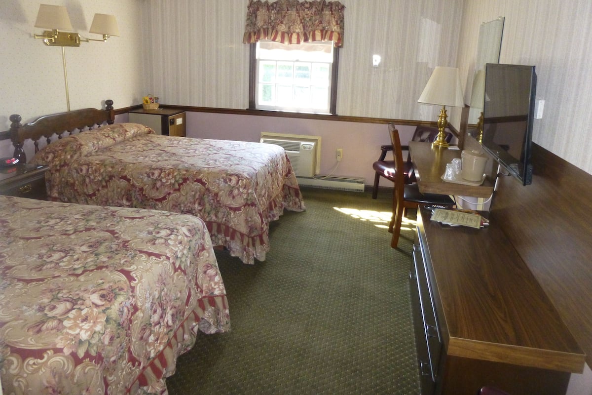 Una habitación de hotel con dos camas, un escritorio con televisor y una ventana con cortinas.