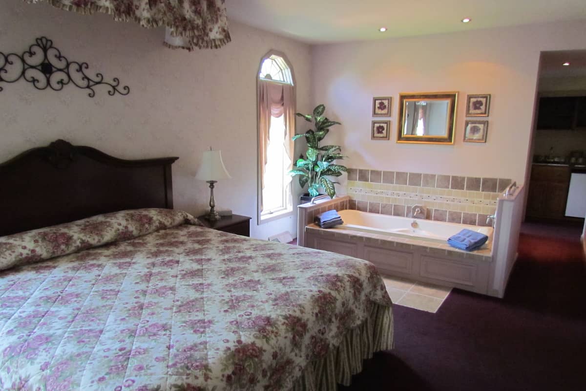 Un dormitorio con una cama grande, un baño con bañera y vistas a la cocina.