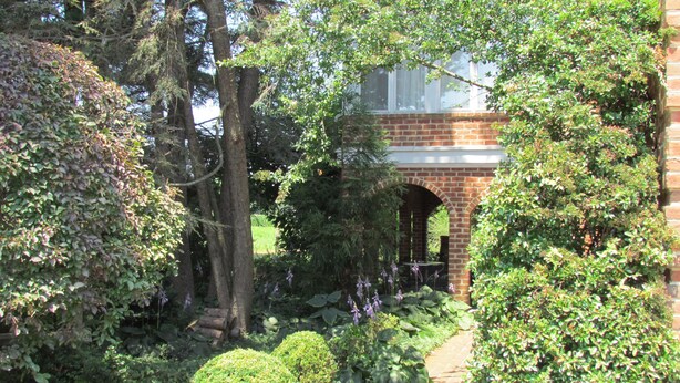 A garden pathway leading to a brick archway with a view of a building. - Smoketown Inn (Smoketown)