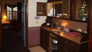 A kitchen with wooden cabinets, a countertop with various items, a trash can, and a dining area with a table and chairs. - Smoketown Inn (Smoketown)