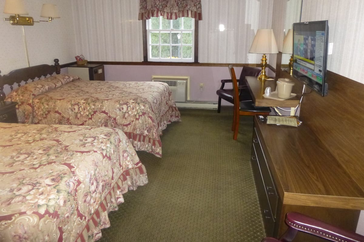 Una habitación de hotel con dos camas, un escritorio, una silla, un ventanal y un televisor.