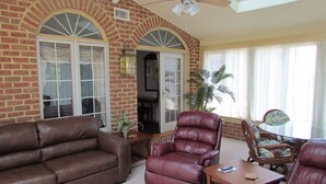 A living room with a brick wall, a brown leather sofa, a leather armchair, and a wooden coffee table. - Smoketown Inn (Smoketown)