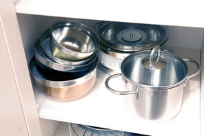 Une cuisine équipée d’ustensiles de cuisine et de couvercles en acier inoxydable, rangés sur une étagère blanche.