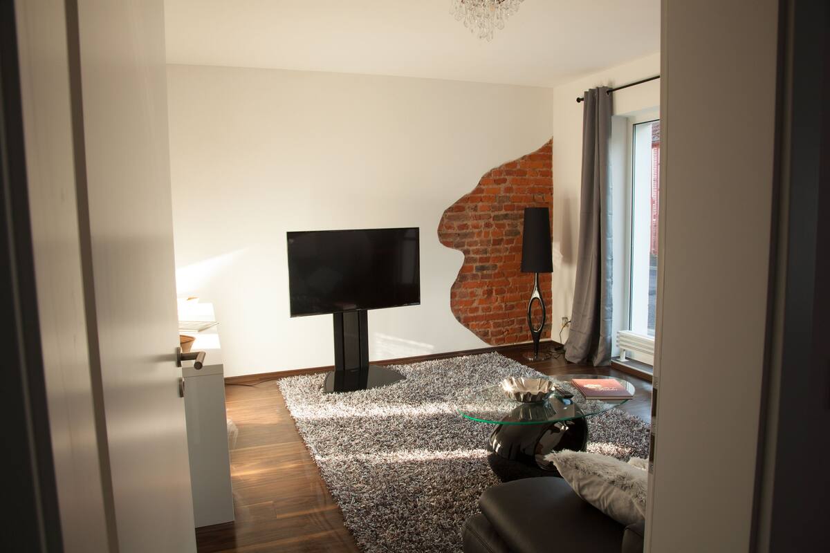 Ein modernes Wohnzimmer mit Fernseher, Glastisch und einer gemütlichen Sitzecke.