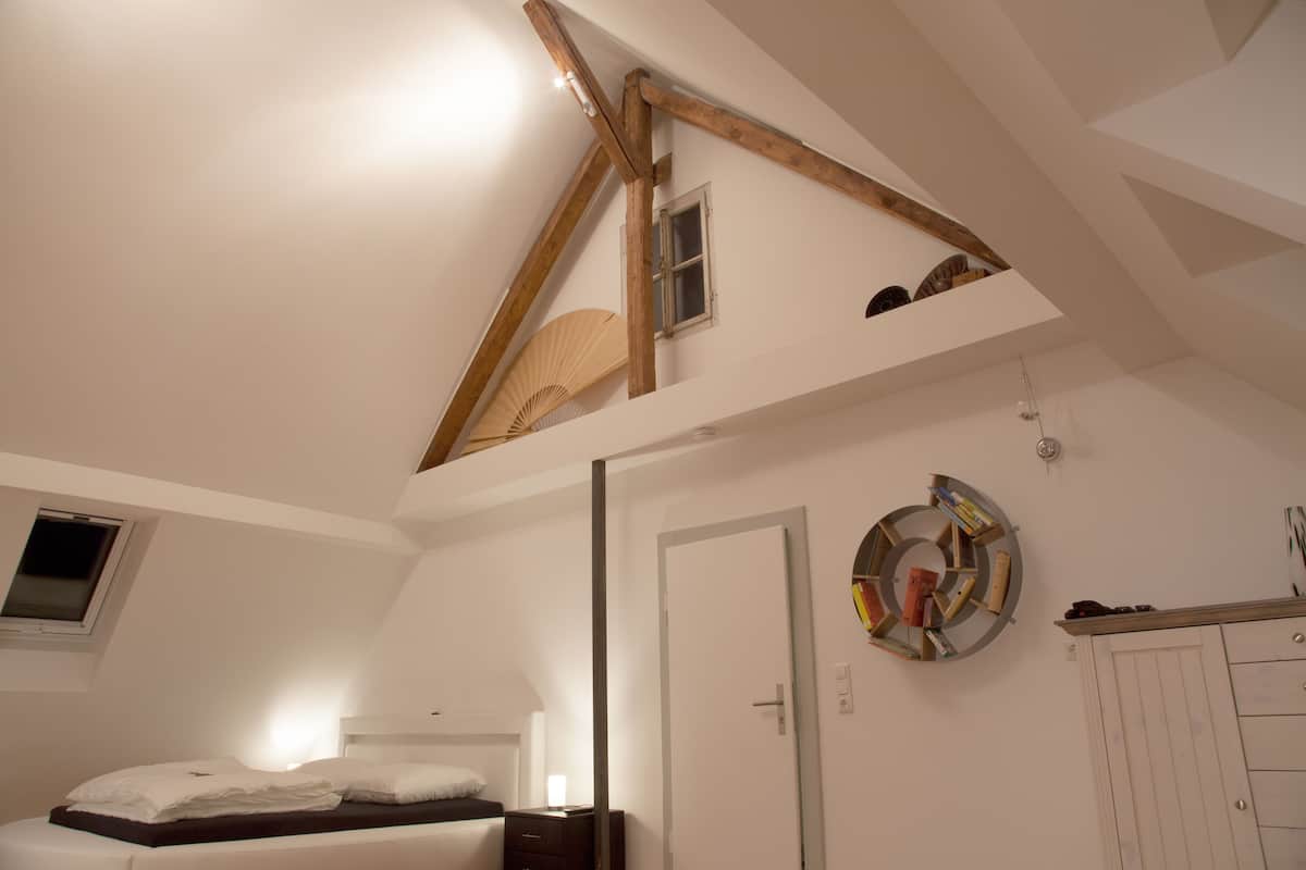 Ein Schlafzimmer mit schrägen Wänden, einem Bett, einem Nachttisch, einem Spiegel und einem Kleiderschrank.