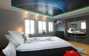 A modern bedroom with a bed, two windows, a large mirror, and a ceiling mural of space. - Gästehaus Fulda (Fulda)