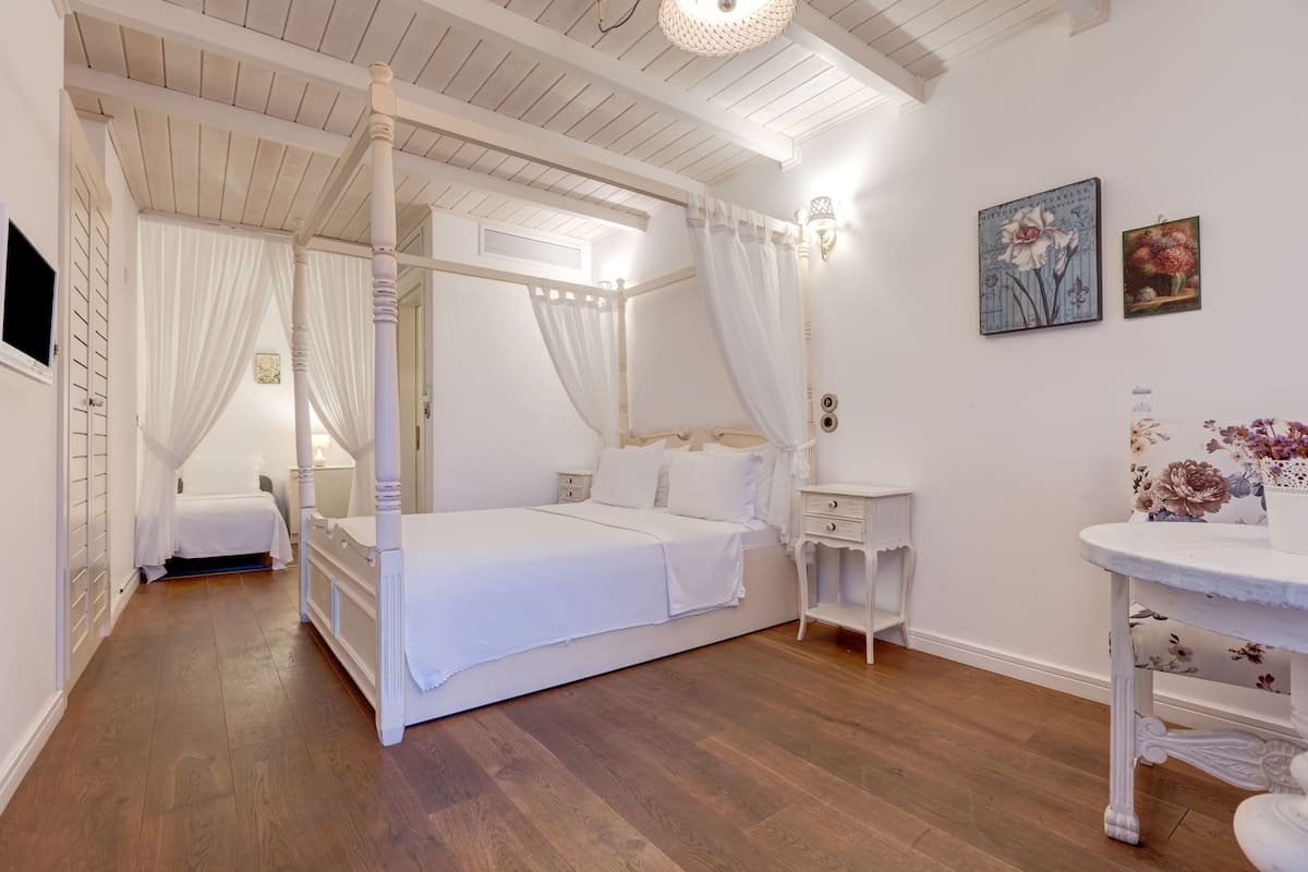 A four-poster bed with a canopy, a bedside table, a nightstand, and a small round table with a floral vase.