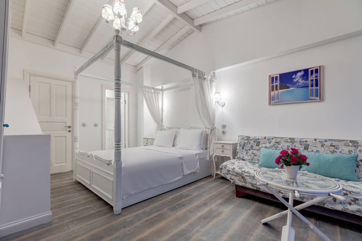 A bedroom with a four-poster bed, a sofa with a glass coffee table, and a painting of a beach scene.