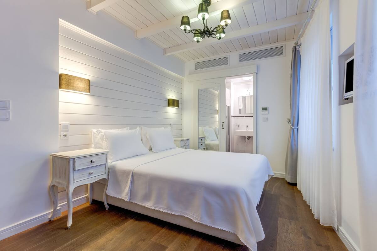 A bedroom with a large bed, a nightstand, a mirror, and a ceiling light fixture.