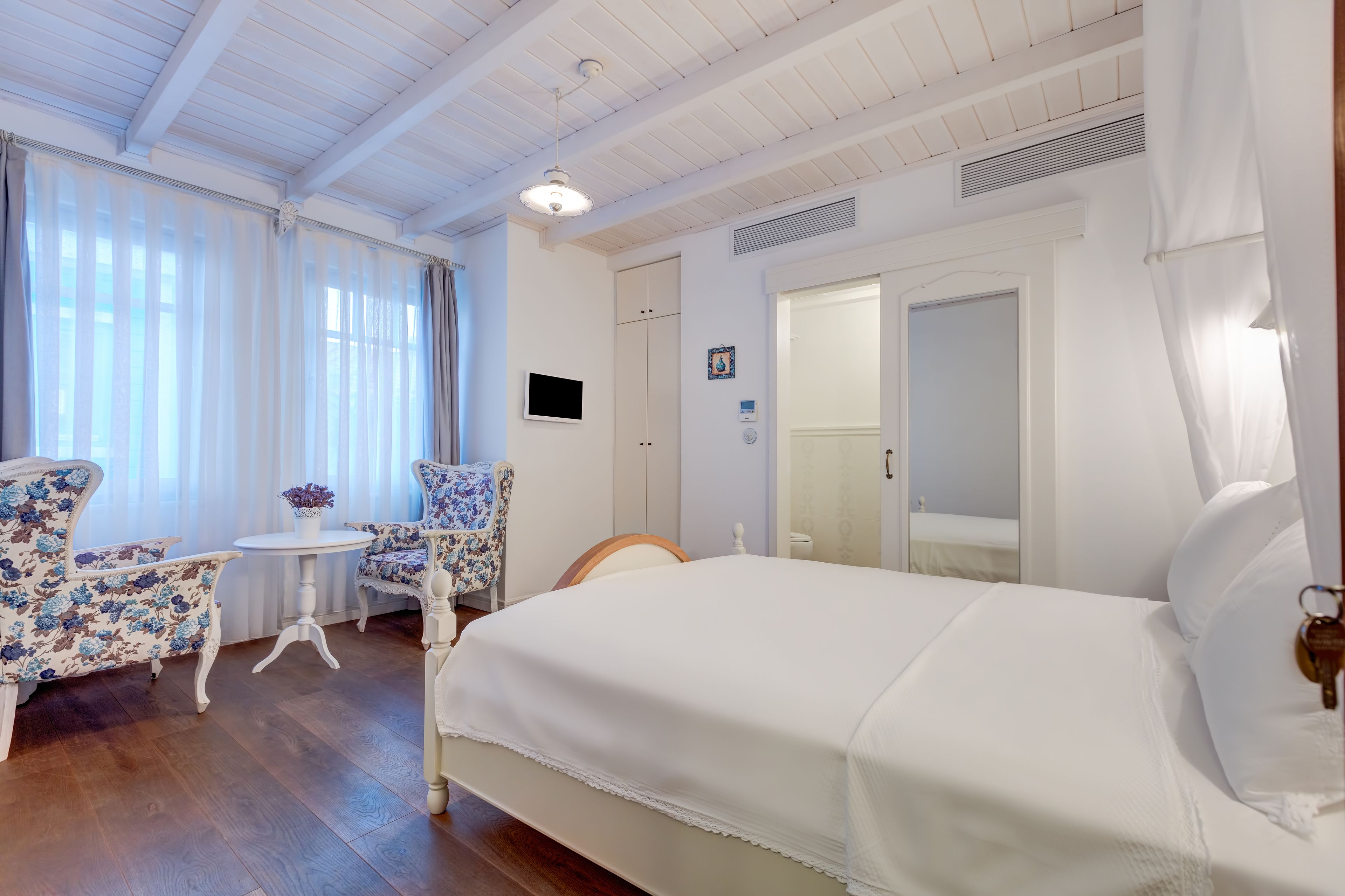 A hotel room with a bed, a small table with chairs, and a window with curtains.