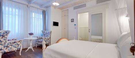 A hotel room with a bed, a small table with chairs, and a window with curtains.