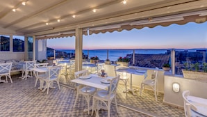 Una terraza con mobiliario blanco y vista al mar al atardecer.